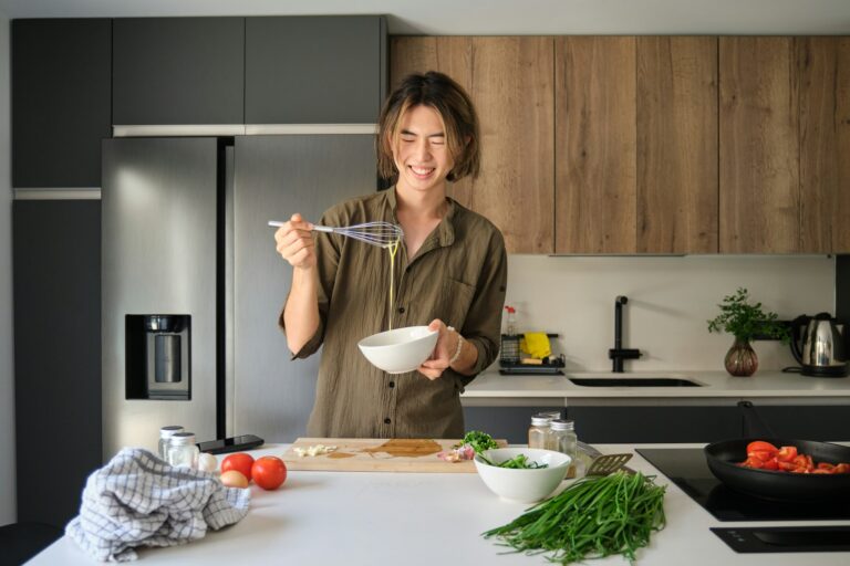 Asian young man beating eggs at kitchen.